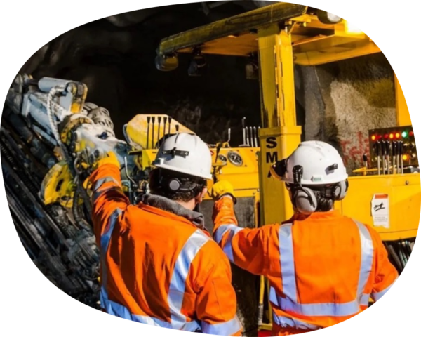 two miners talking in front of machinery.