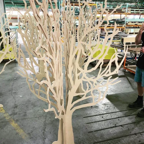 a man standing next to a wooden sculpture of a tree.