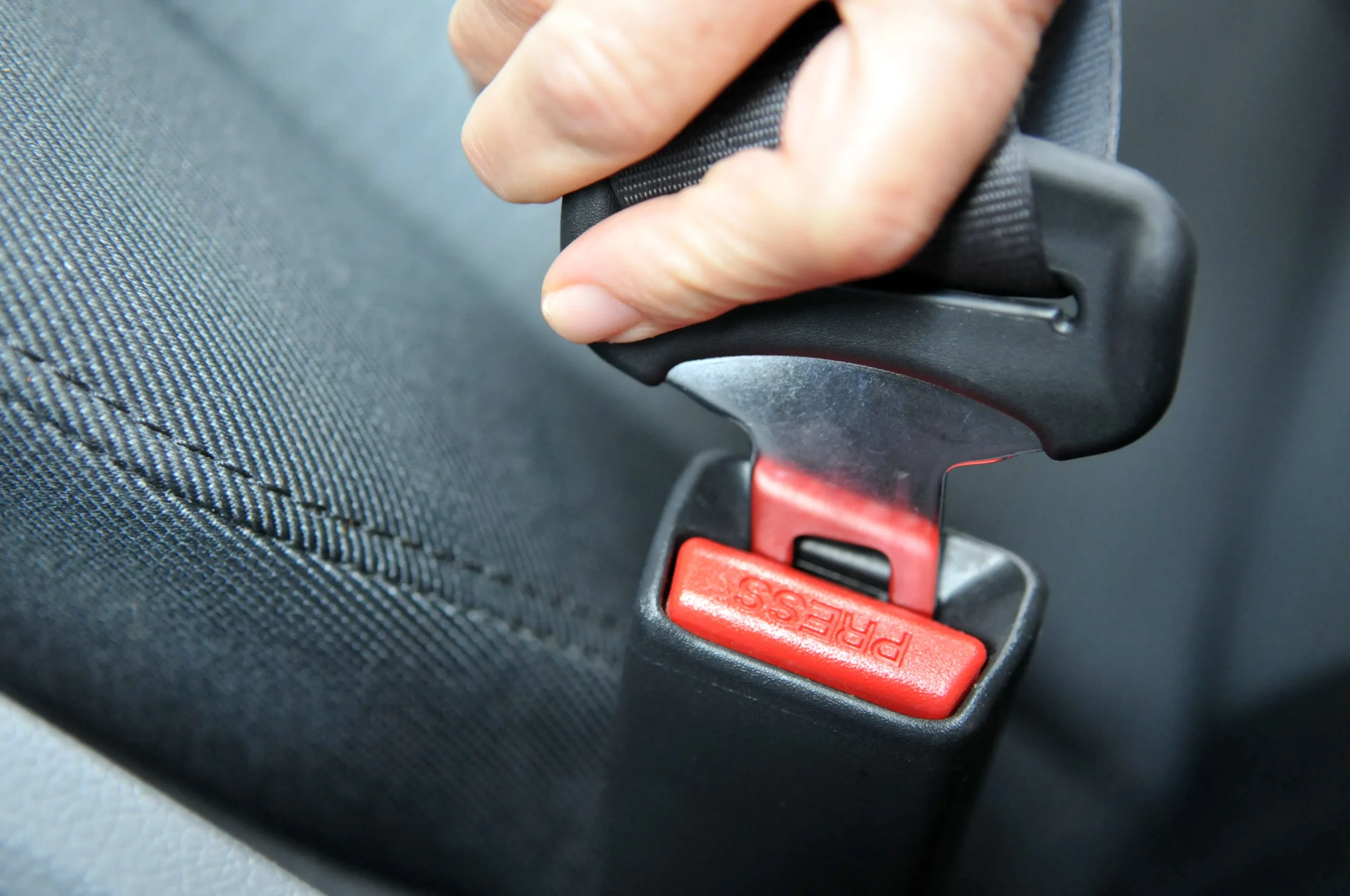 a hand holding a red and black seat belt in a car.