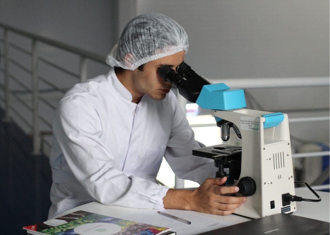 a man in a white lab coat looking through a microscope.